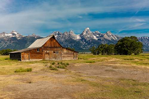 A horizontal fine art landscape photograph of the historic wooden T.A. Moulton Barn on Mormon Row in Grand Teton National Park, backdropped by the jagged, snow-capped mountain peaks of Wyoming.