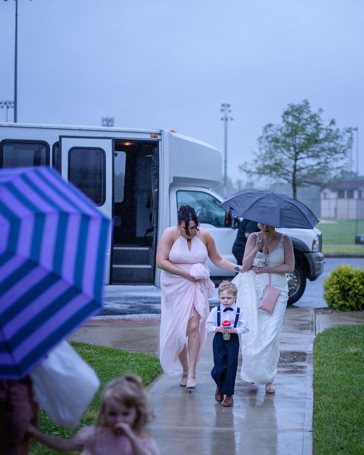 bride on the sidewalk of ross station after stepping of the bus, hiding under umbrella on a rainy wedding day