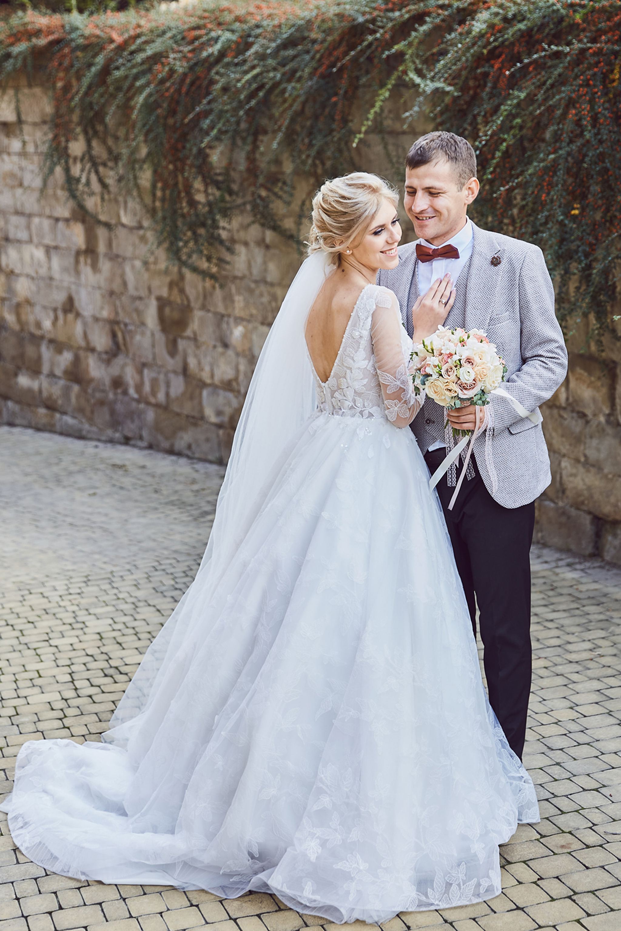 Bride and groom embracing beside an ivy-covered stone wall