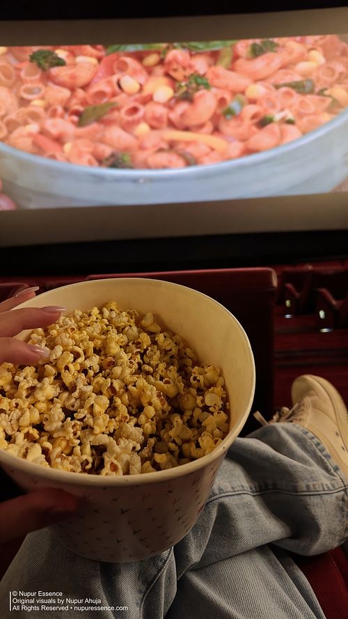 Close-up popcorn bucket during a movie screening with Nupur Ahuja in white top and denim jeans, published through Nupur Essence