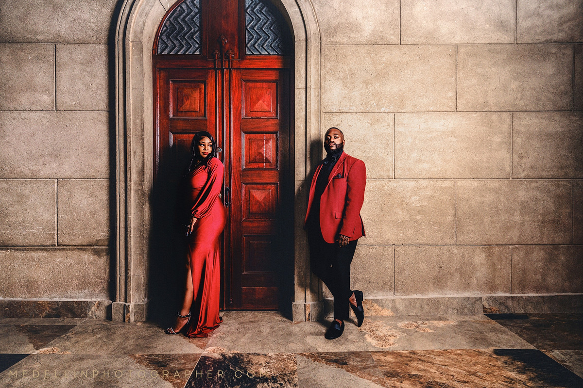 Two portraits of a couple in red beside a carved wooden door in Medellin