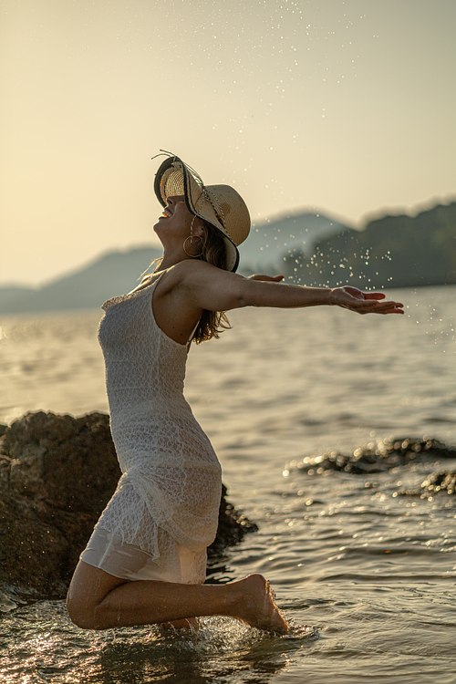 Femme agenouillée dans la mer les bras ouverts lors d’une séance photo à Hyères