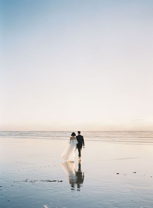 Beautiful vertical back shot of a newly wed couple walking barefoot on the beach