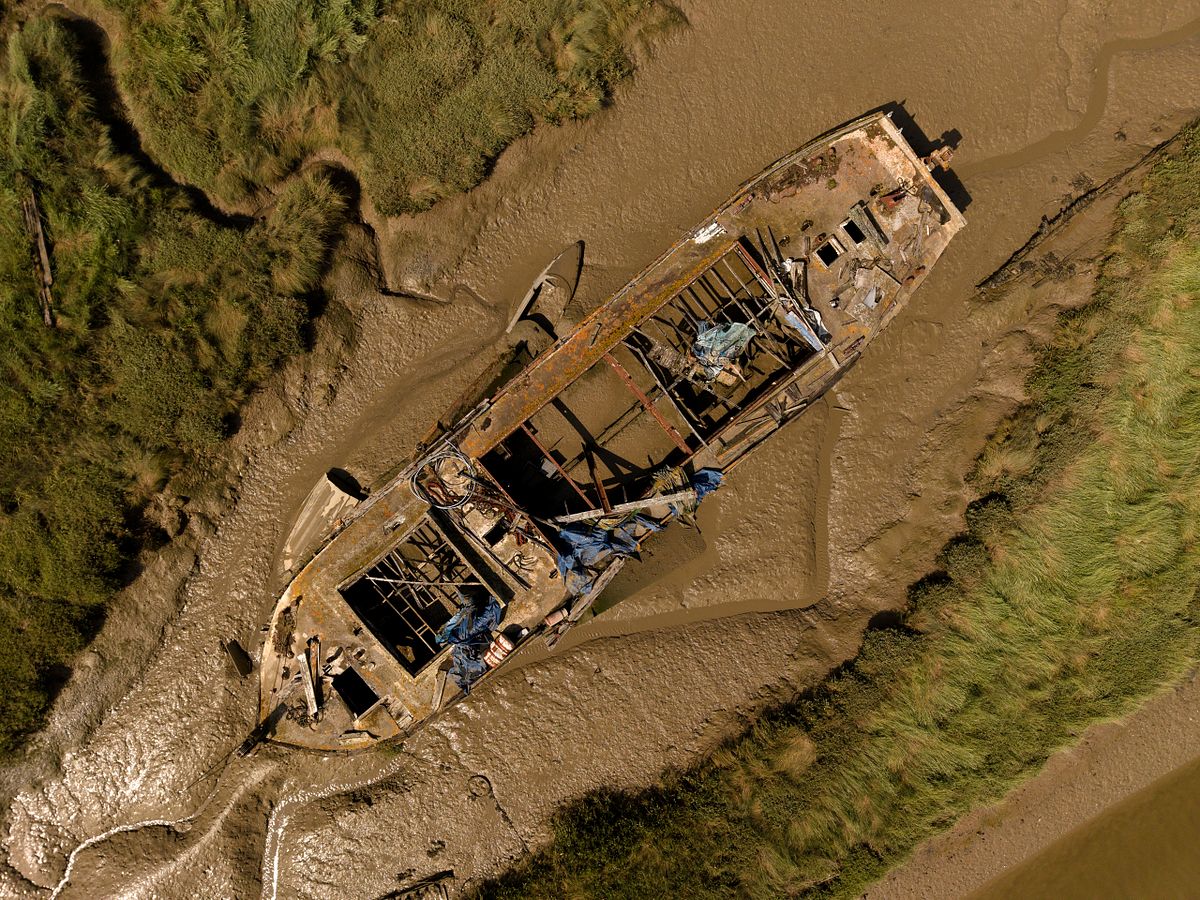 Aerial photograph of an abandoned boat wreck in the tidal mudflats of East Haven Creek, Benfleet, Essex, surrounded by saltmarsh and winding creeks.