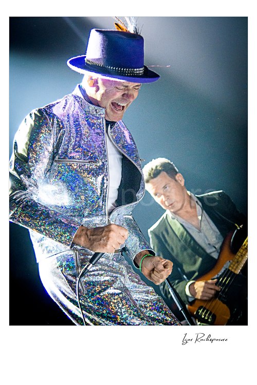 Gord Downie Tragically Hip Live Concert Print  Vertical color image of Gord Downie of The Tragically Hip in a dramatic live performance moment, wearing a glittering silver suit and purple hat with Gord Sinclair visible behind him on bass