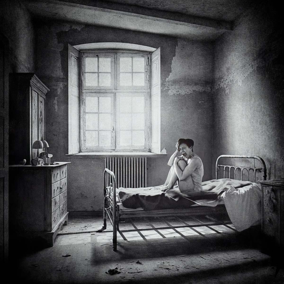 photo tarot The Asylum, femme en camisole hurlant dans une chambre sombre d&rsquo;asile ancien, &eacute;clair&eacute;e par une lumi&egrave;re crue