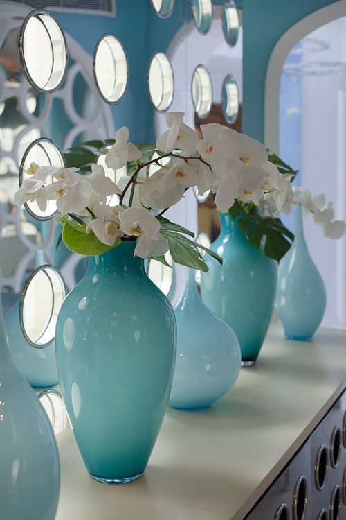 Détail de vases turquoise en verre avec bouquet d’orchidées blanches sur un meuble. Photographie de détails décoratifs par Nicolas Karadimos.