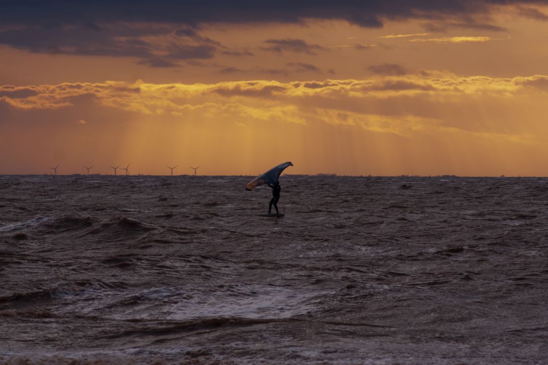 Wing foiler riding across the sea at sunset near Snettisham on the Norfolk coast.