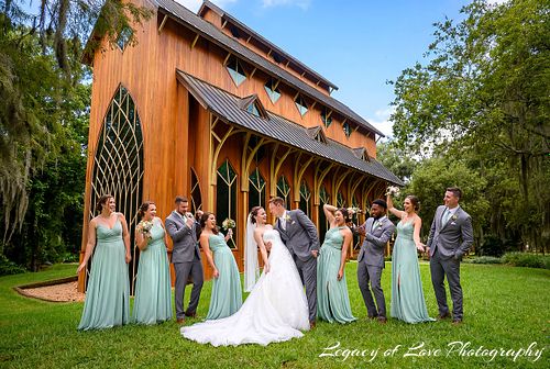 Large joyful wedding party in navy suits and emerald green dresses posing outside the Baughman Center in Gainesville.