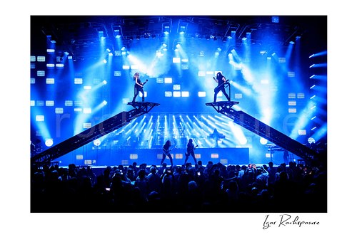 Horizontal color image of Trans Siberian Orchestra performing on stage with guitarists on elevated platforms above a packed arena crowd