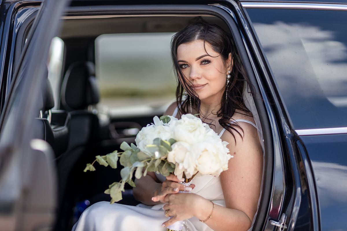 Bride sitting in a car holding her white wedding bouquet