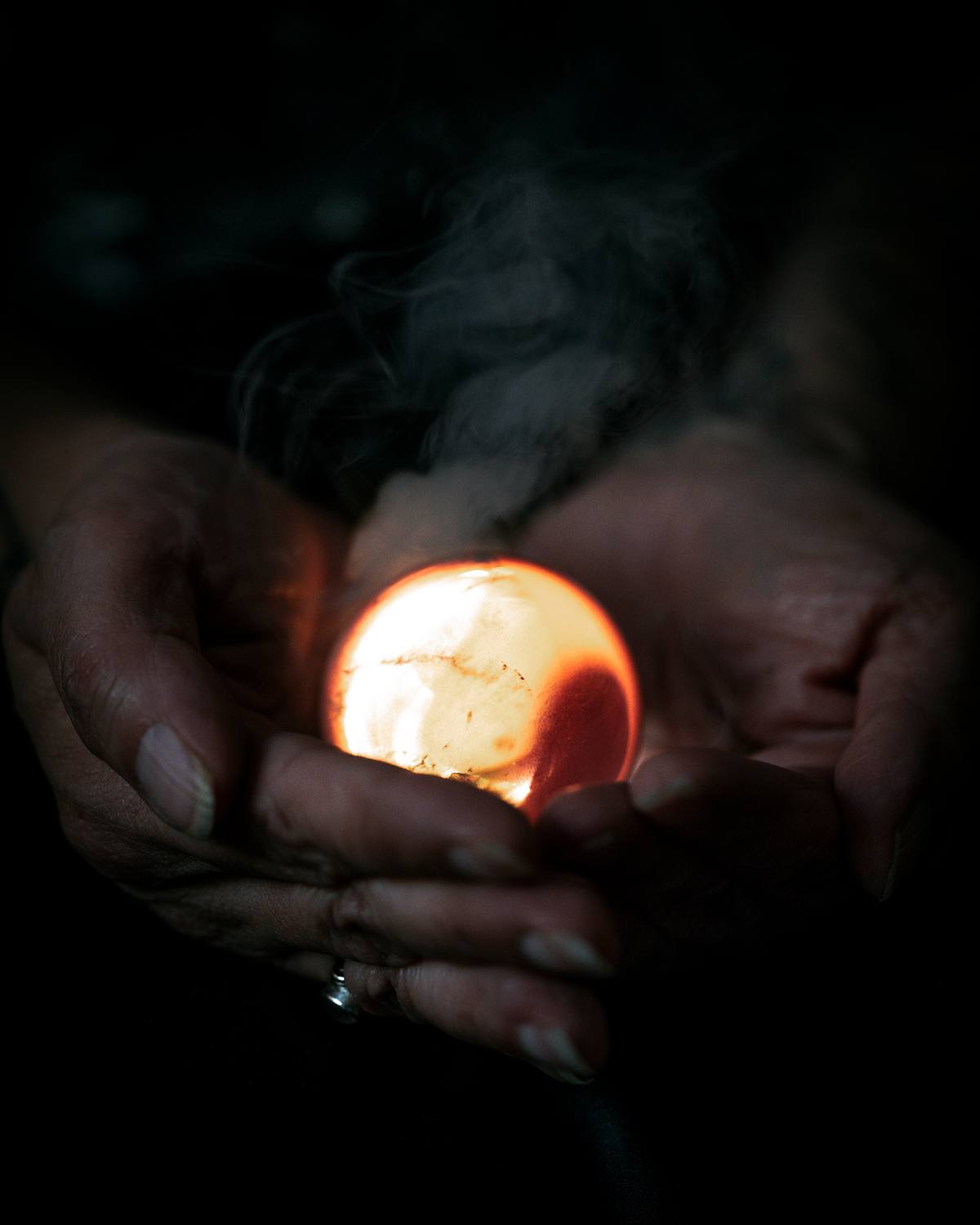 Hands holding a glowing orb in a dark space.