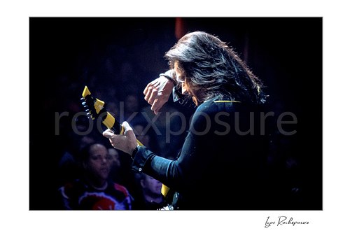 Horizontal color image of Michael Sweet of Stryper performing live with a black and yellow striped guitar in a dramatic stage portrait