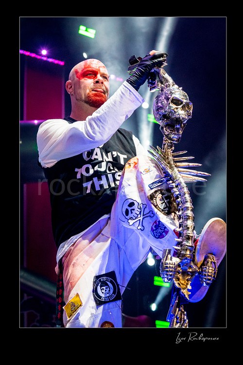Vertical color image of Ivan Moody of Five Finger Death Punch holding a skull-covered microphone stand under bright stage light