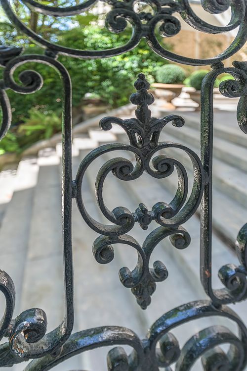 Détail de balustrade en fer forgé ouvragé avec vue sur le jardin depuis un appartement haussmannien de 400 m² rue du Faubourg Saint-Honoré. Photographie d’architecture intérieure par Nicolas Karadimos.