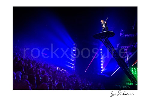 Horizontal color image of Chris Caffery of Trans Siberian Orchestra performing on a raised platform above the arena crowd in blue stage light