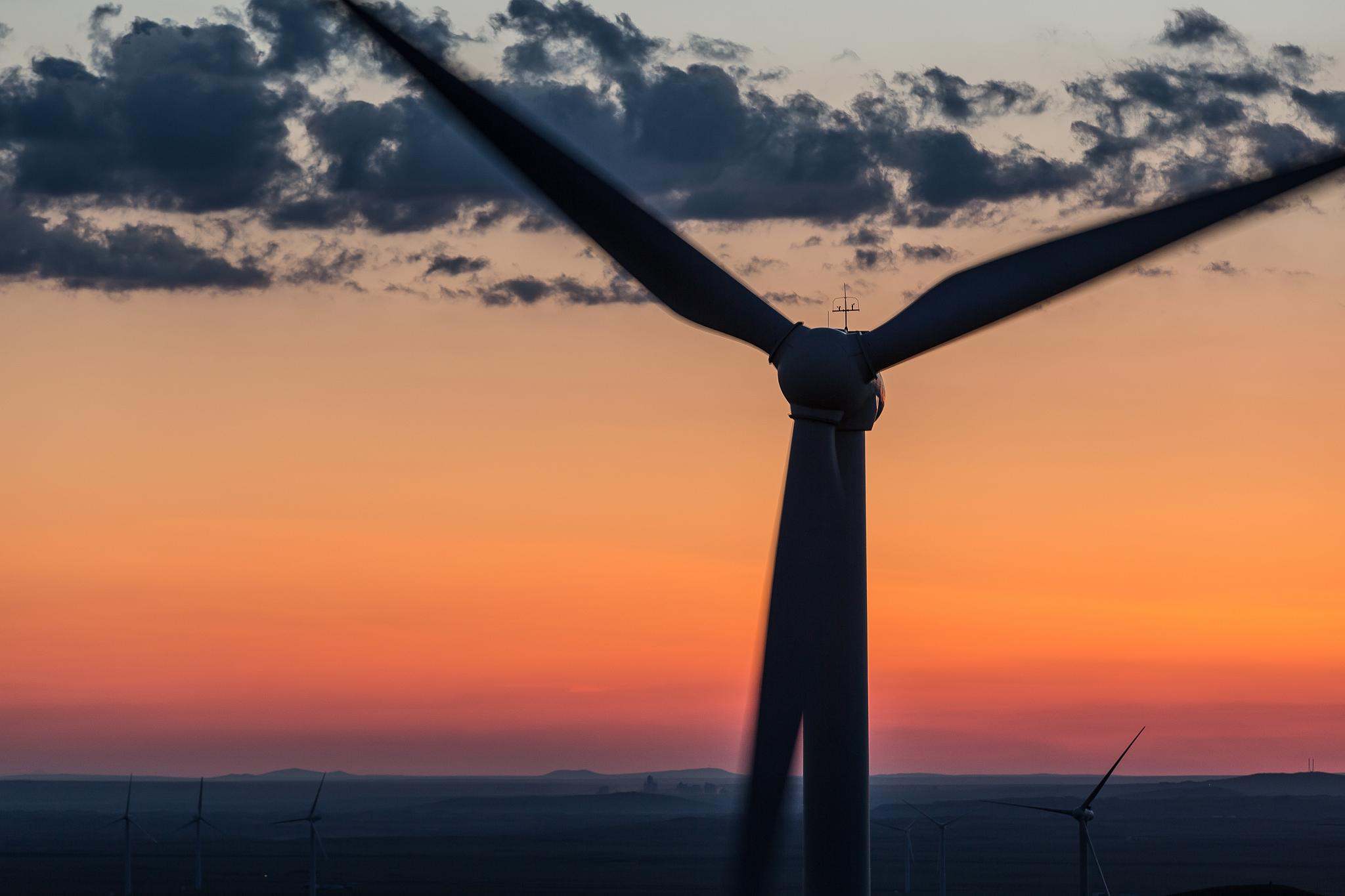 A silhouetted wind turbine against a sunset near Xilinhot, Inner Mongolia, China.