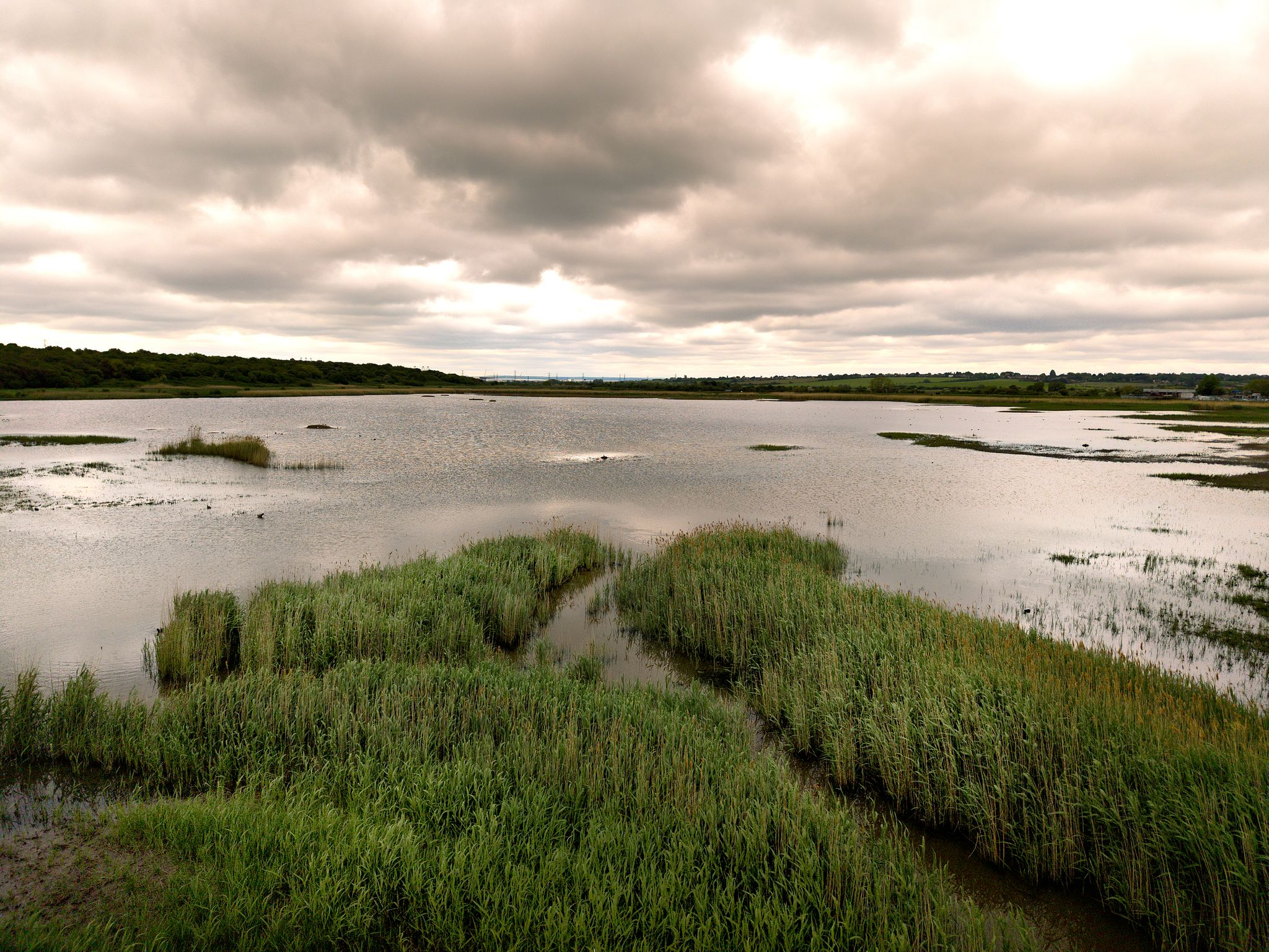 Aerial photograph of calm tidal Essex masrshland and winding waterways beneath dramatic cloudy skies along the coastline