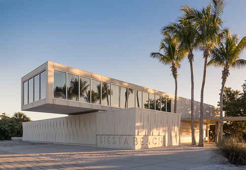 Architectural photography of the modern Siesta Key Pavilion in Sarasota, Florida, featuring its sleek concrete canopy, glass walls, and surrounding palm trees at the beach.