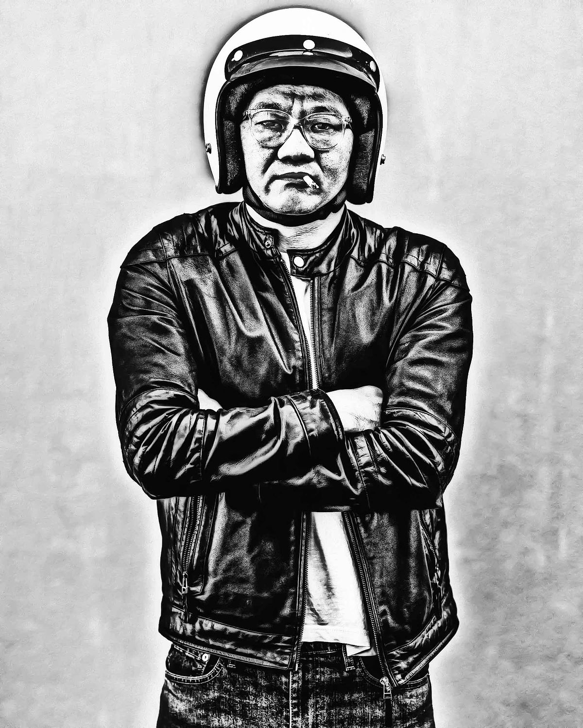 Portrait of an Asian man in a motorbike helmet smoking a small cigarette. Dressed in black leather jacket. Arms crossed.