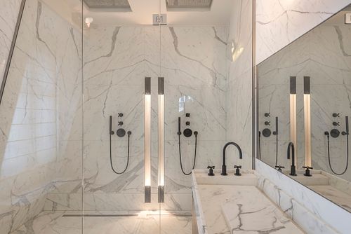 Salle de bains en marbre blanc avec douches à l’italienne et robinetterie noire dans un appartement haussmannien sur les Champs-Élysées, Paris. Photographie d’architecture intérieure par Nicolas Karadimos.