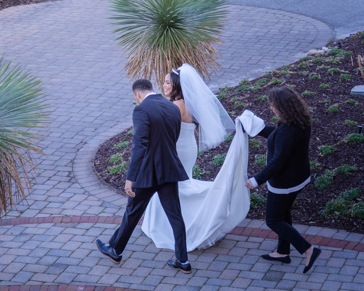 bride and groom walking away after ceremony with the wedding planner holding the train at baywood weddings in Millsboro, DE