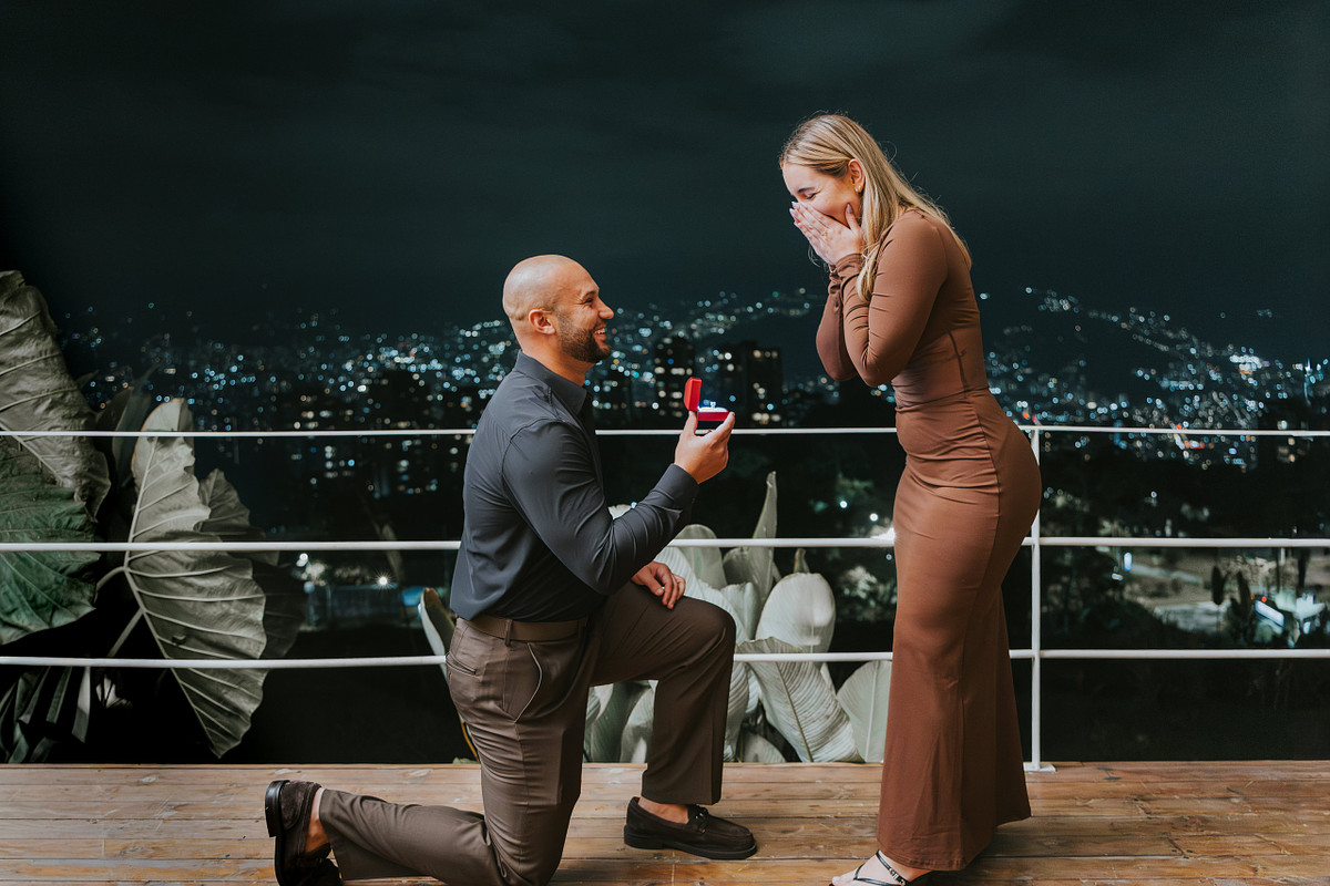 Man kneeling with a ring box during a surprise proposal on a Medellin balcony at night