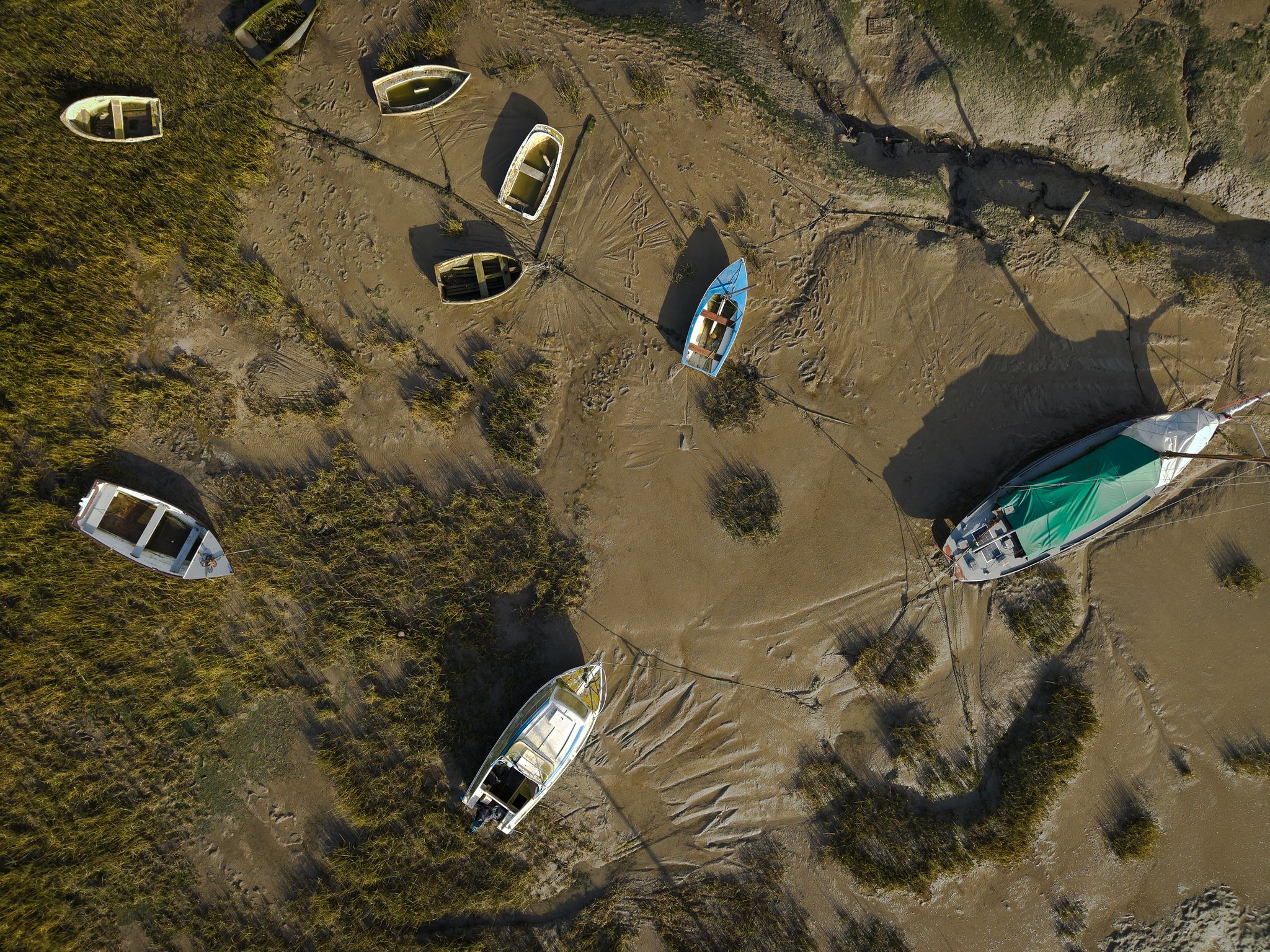 Aerial drone photograph of scattered boats resting on exposed tidal mudflats at low tide along the coastline.