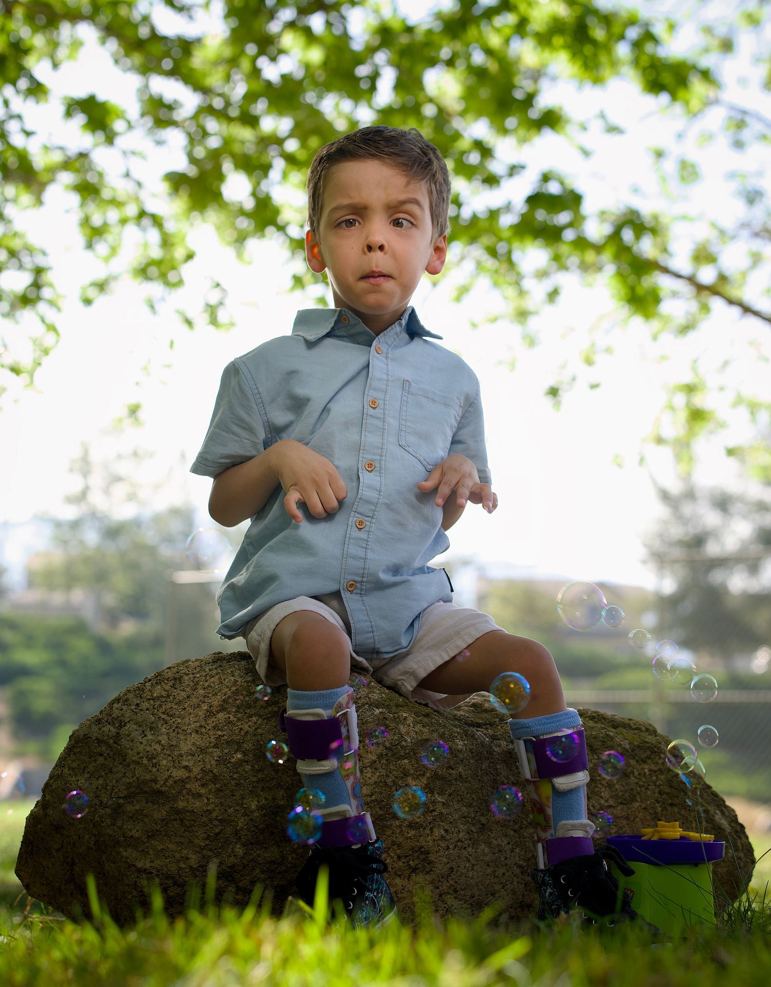 Young child seated on a rock in soft green light during a portrait session.