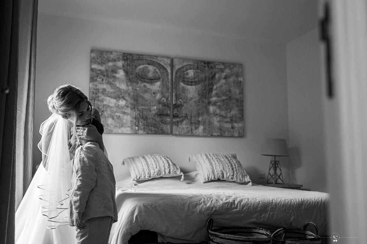 Un &eacute;change &eacute;motionnel dans une chambre &eacute;clair&eacute;e naturellement, o&ugrave; la mari&eacute;e enlace tendrement son jeune fils, avec une &oelig;uvre d'art murale cr&eacute;ant une atmosph&egrave;re sereine, symbolisant l'affection familiale lors du mariage &agrave; N&icirc;mes