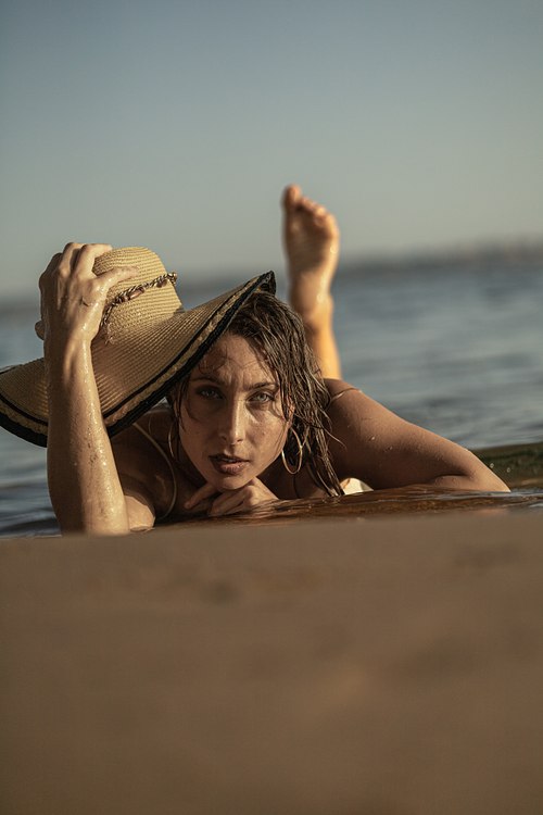 Portrait d’une femme au chapeau apparaissant derrière un rocher sur une plage de Hyères
