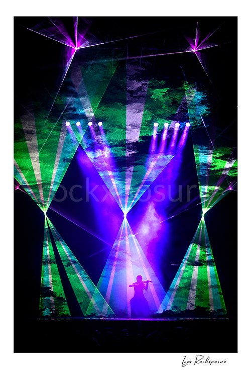 Vertical color image of a Trans Siberian Orchestra violinist Roddy Chong performing in silhouette beneath purple and green laser lights
