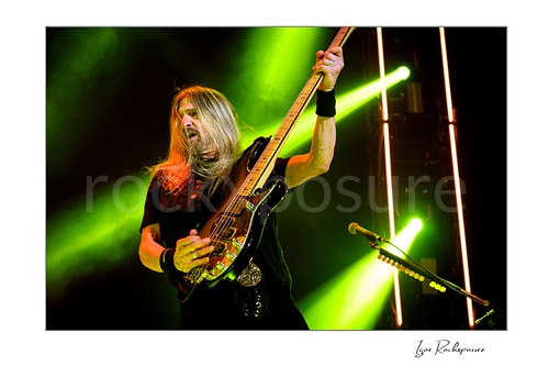Horizontal color image of James LoMenzo of Megadeth playing bass on stage with vivid green concert lights