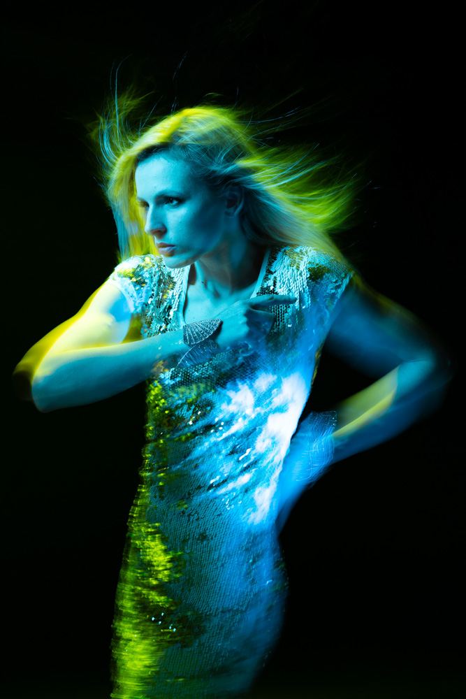 Studio portrait of a woman using various photographic techniques including gelled lights and a dragged shutter to create a blurry effect
