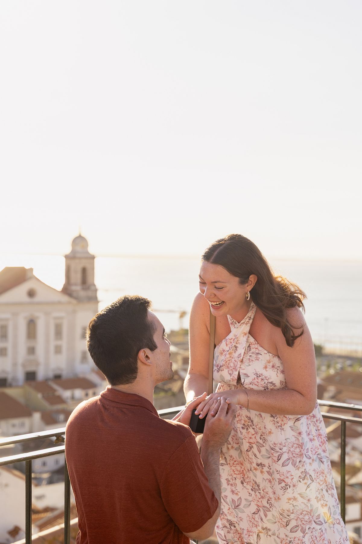 Man proposing to a smiling woman at a Lisbon viewpoint overlooking Alfama