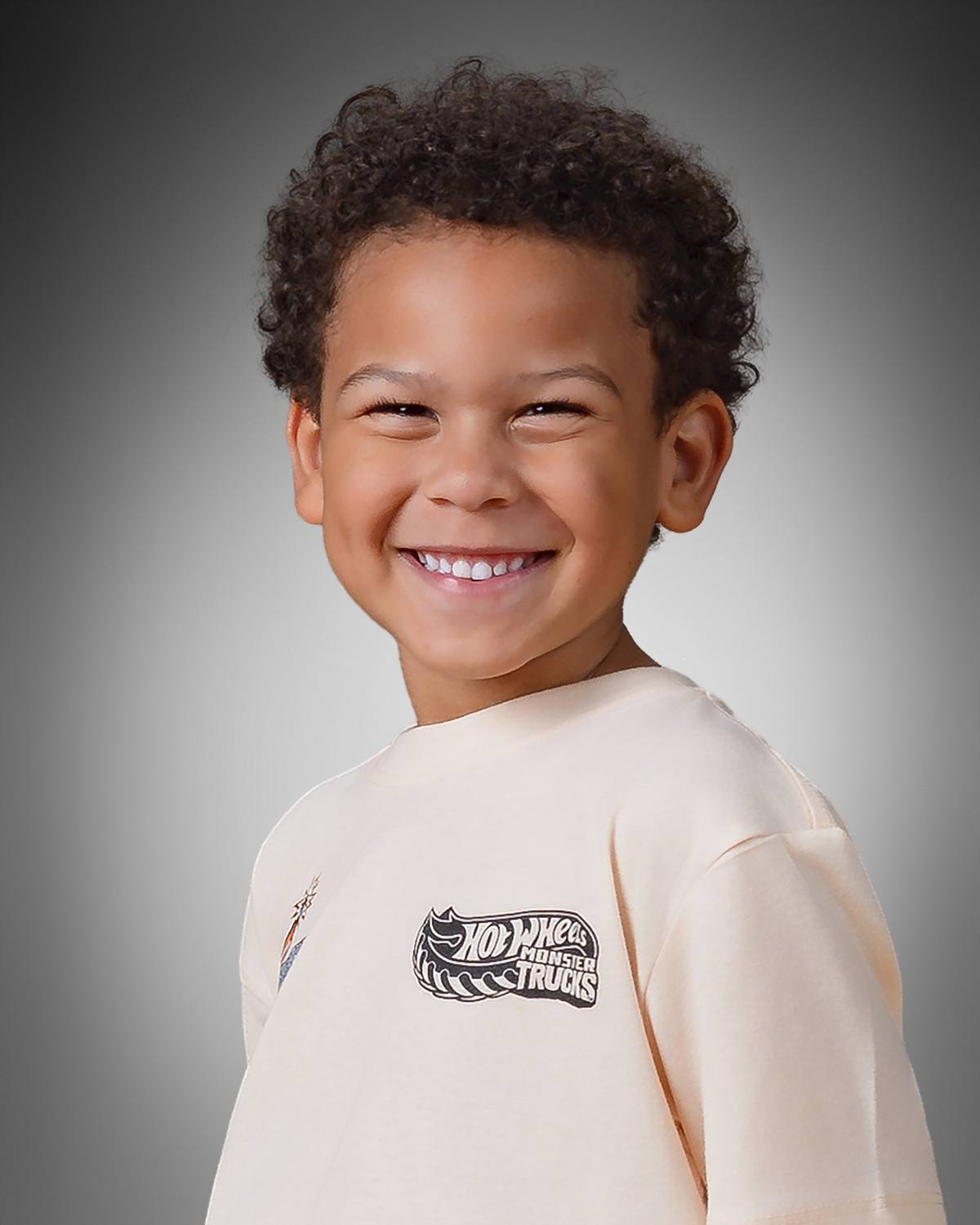 Preschool child portrait wearing Hot Wheels Monster Trucks shirt on gray studio background