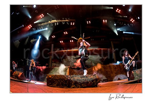 Adrian Smith and Steve Harris of Iron Maiden performing live on stage beneath a large airplane stage prop with smoke effects and dramatic concert lighting.