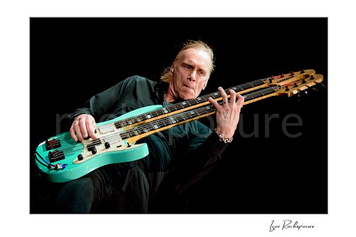 Horizontal color image of Billy Sheehan playing his double-neck bass in a tight low-angle live performance shot