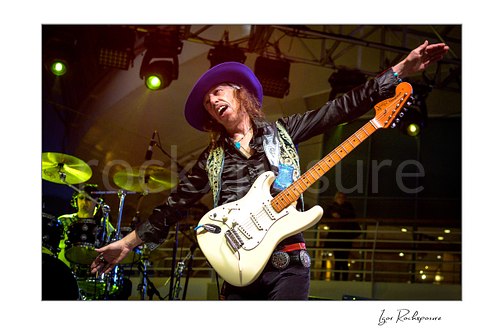 Horizontal color image of Randy Hansen on an outdoor ship deck stage with a white guitar and outstretched arms under green concert lights