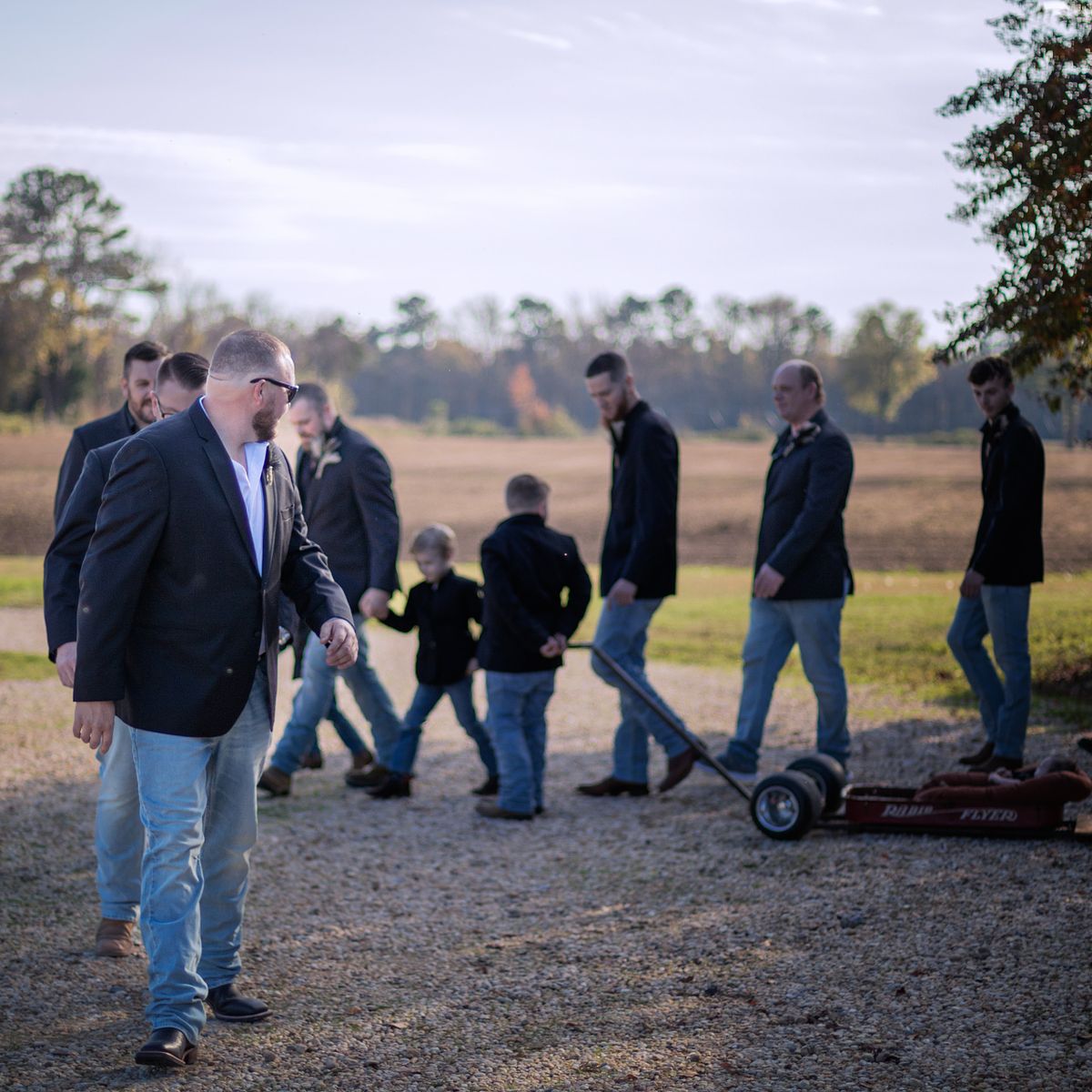 groom and his grooms men are walking toward the wedding ceremony location at cohee farm in williamsburg, md