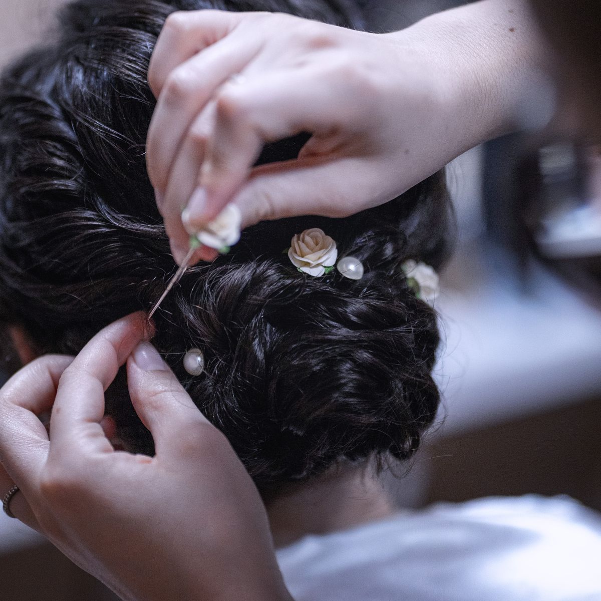 a hair stylist adding pink flower pins to a braided bun.