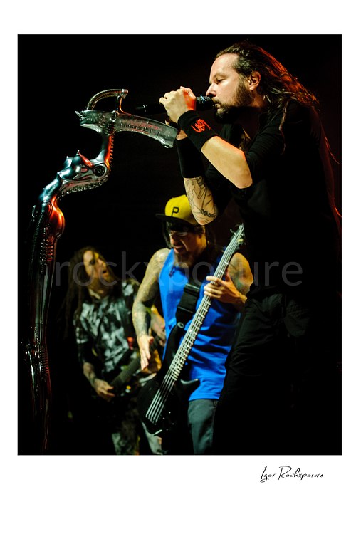 Vertical color image of Korn members Brian “Head” Welch, Fieldy, and Jonathan Davis performing live on stage with Jonathan Davis singing beside his distinctive stage microphone stand