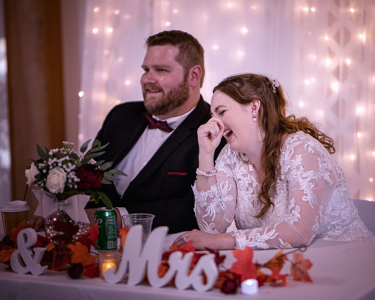couple laughing at the sweetheart table listening to a speech