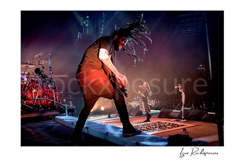 Horizontal color image of Korn members Brian “Head” Welch and Jonathan Davis performing live on stage with Brian “Head” Welch in the foreground and Jonathan Davis near the microphone stand