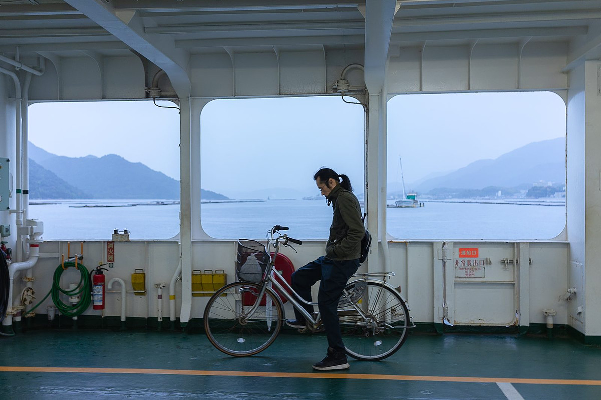 Une personne à vélo sur le pont d'un ferry, la mer dans la brume derrière les vitres