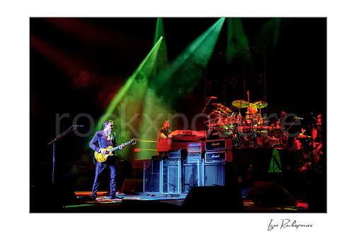 Horizontal color image of Joe Bonamassa performing live on stage with his guitar under dramatic green and red lighting