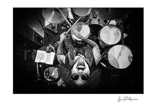 Horizontal black and white image of Frankie Banali in an aerial overhead drummer shot at the drum kit wearing sunglasses during a live performance