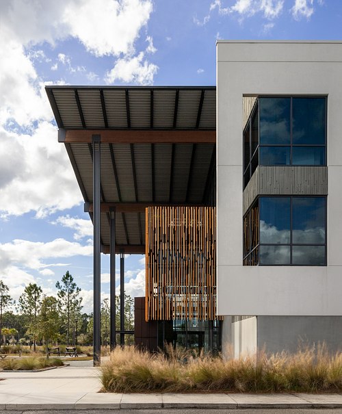A vertical architectural side view of the Rayonier Forestry Headquarters in Wildlight, Yulee, showcasing the contemporary exterior design, timber screens, and modern glass window systems designed by Stanley Wilcox Architects.