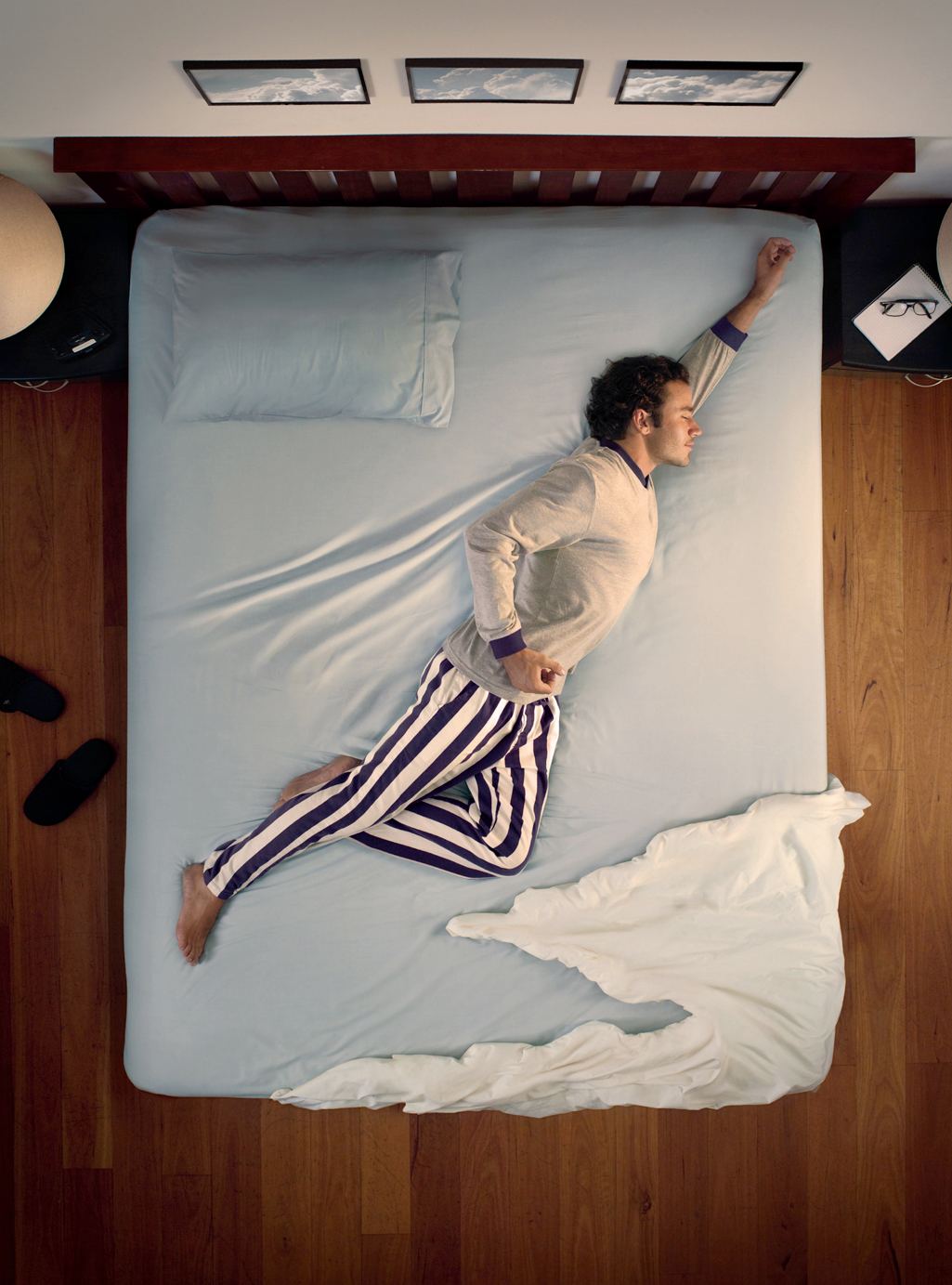 Man in bed sleeps in Superman pose with sheets like clouds for Blackmores