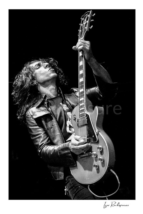 Vertical black and white image of Brent Woods playing guitar on stage in a dramatic upward pose